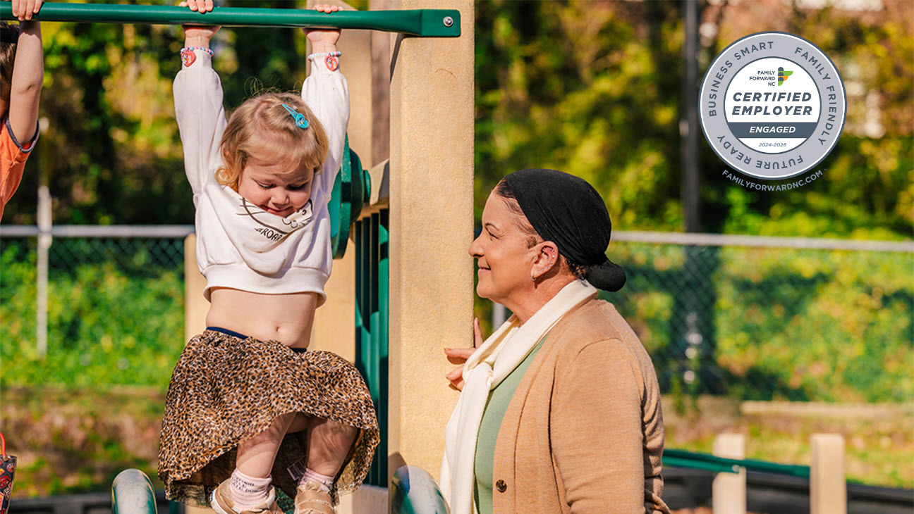 Image of an elderly woman smiling at a young child hanging from a playground bar. A badge signifying family forward certification is embedded in the upper right corner.